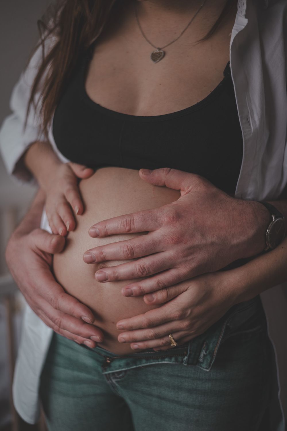 Intimate maternity photo showing hands cradling a pregnant belly in black top and jeans.