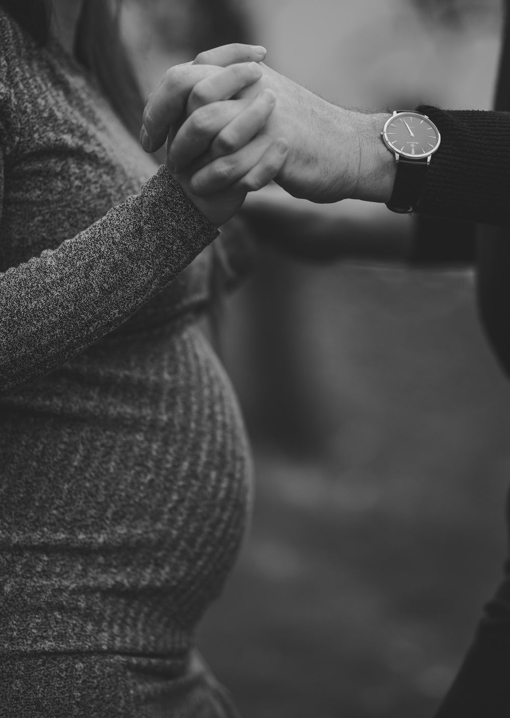 Black and white photo of clasped hands resting on pregnant belly.