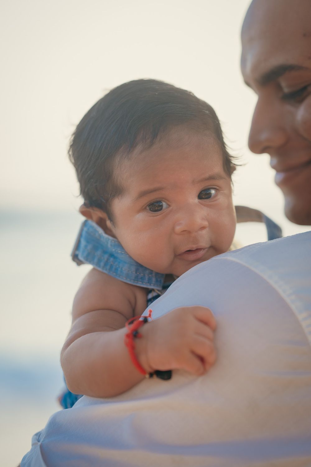 Close-up portrait of baby in white clothing at seaside.