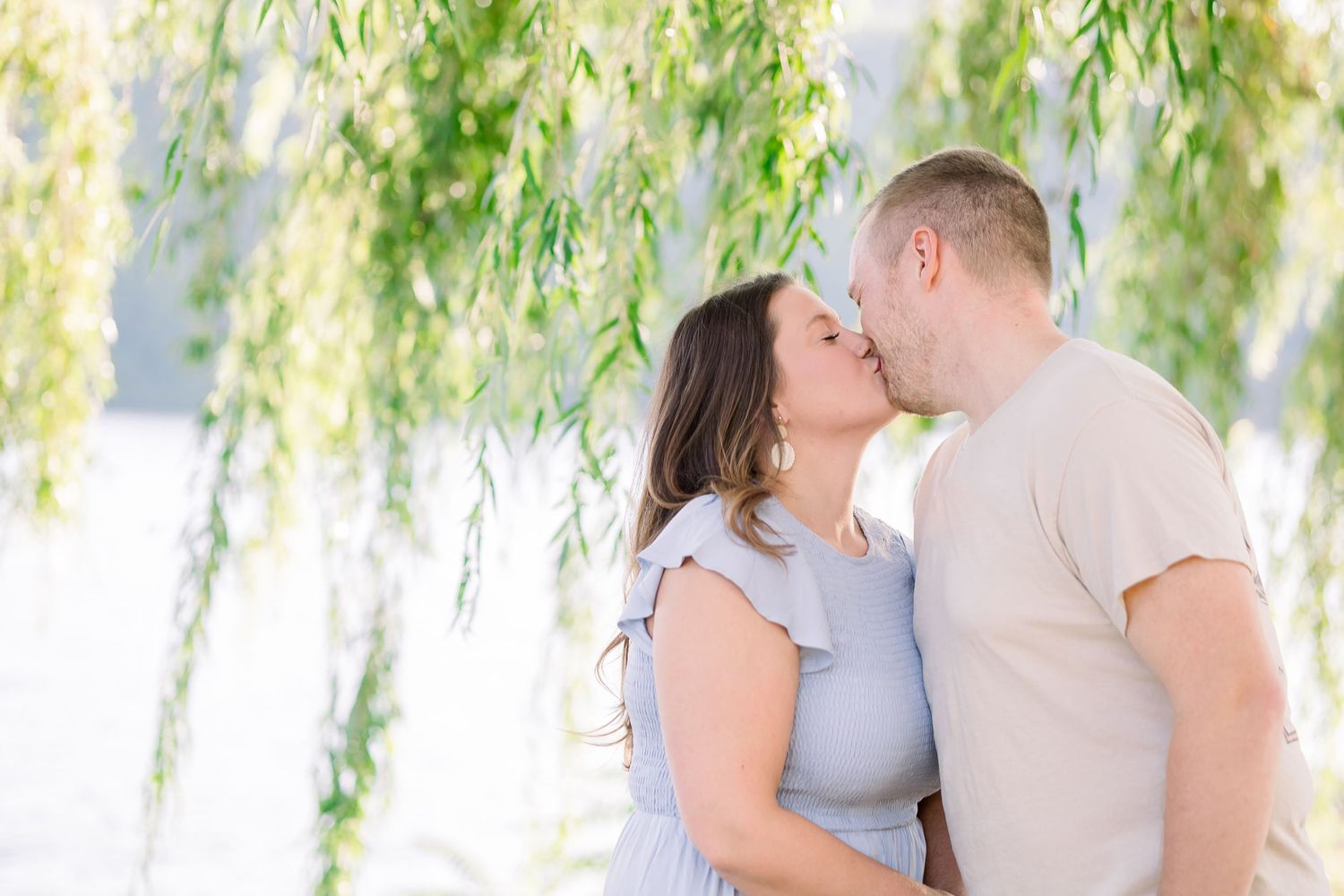 Romantic outdoor photoshoot with soft lighting under willow trees by the water.