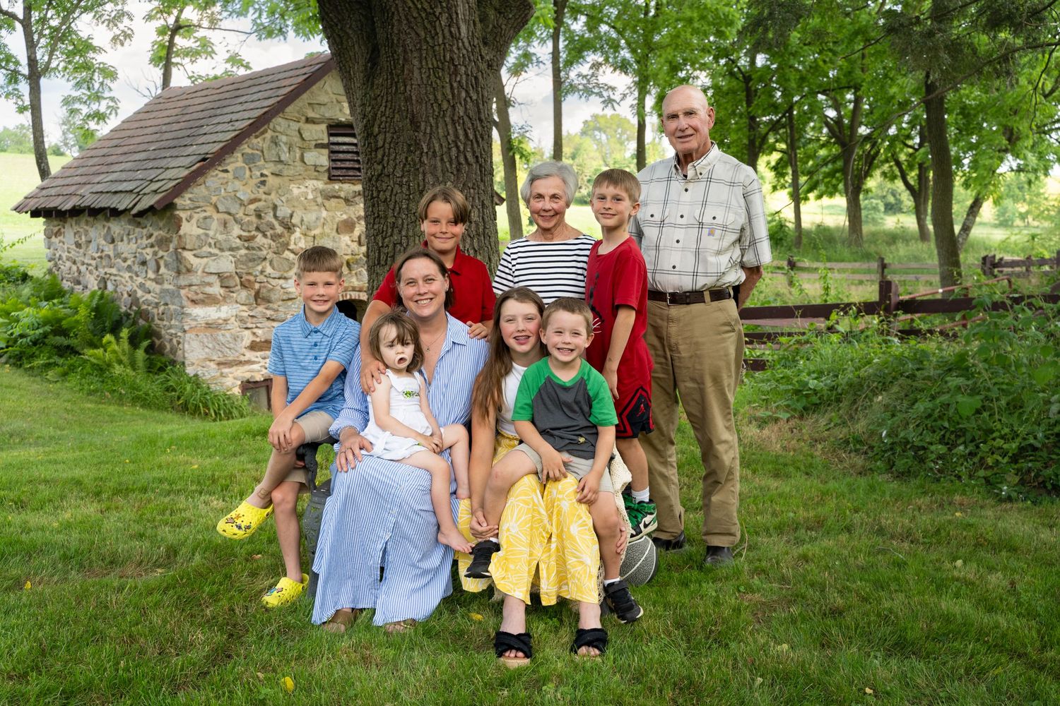 A large family group poses together on the grass in front of a rustic stone building.