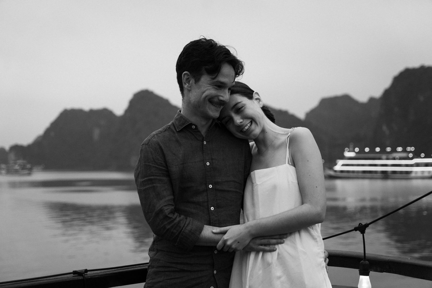 A couple embraces while enjoying a romantic moment against a backdrop of misty mountains and calm waters.