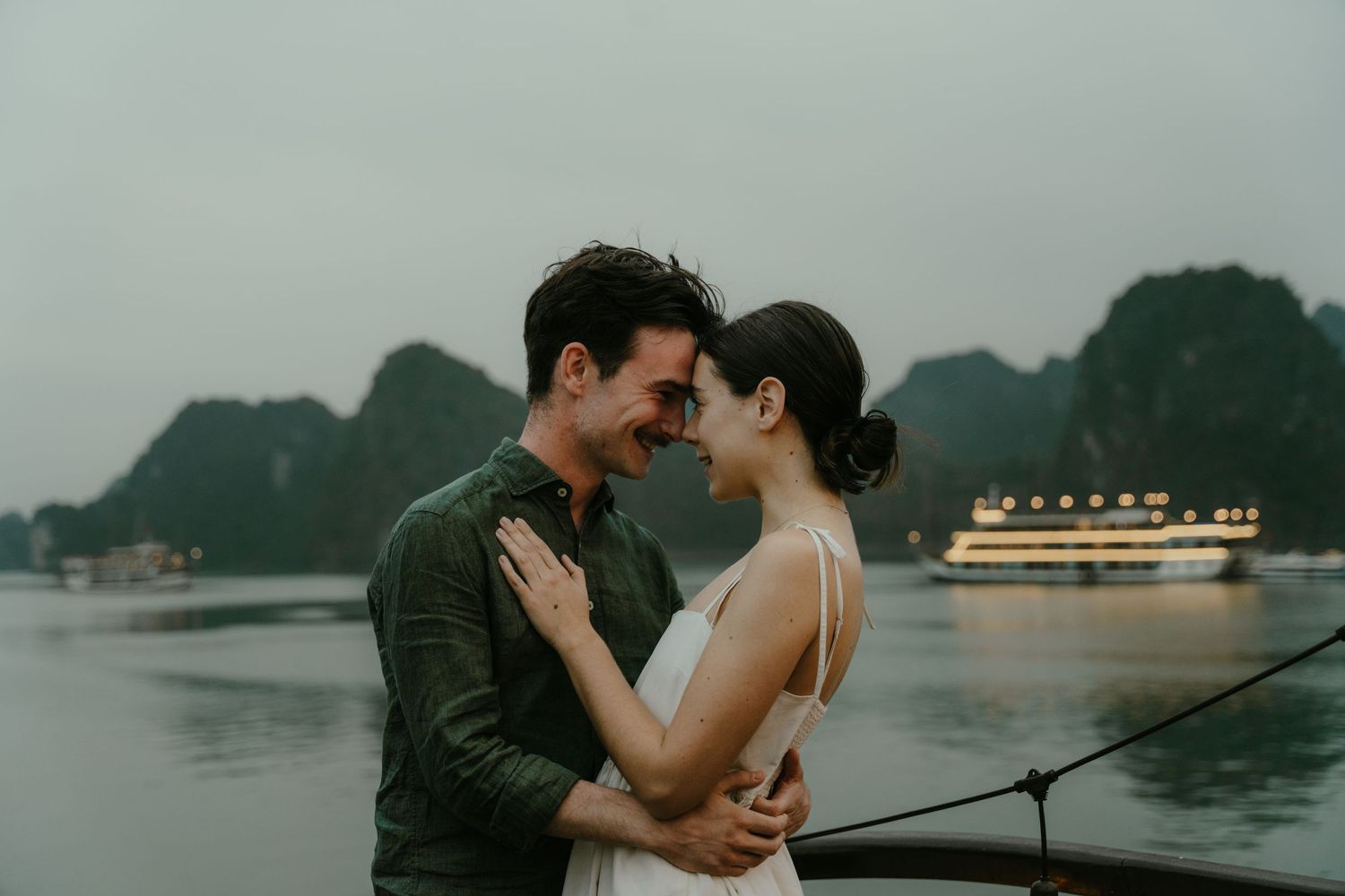 Intimate moment between couple on boat deck with moody mountains and cruise ship in background.