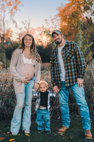 A family in casual fall attire poses together in a field during golden hour sunset.