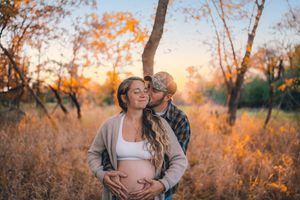 A couple shares an intimate moment during a sunset maternity photoshoot in a golden autumn field.