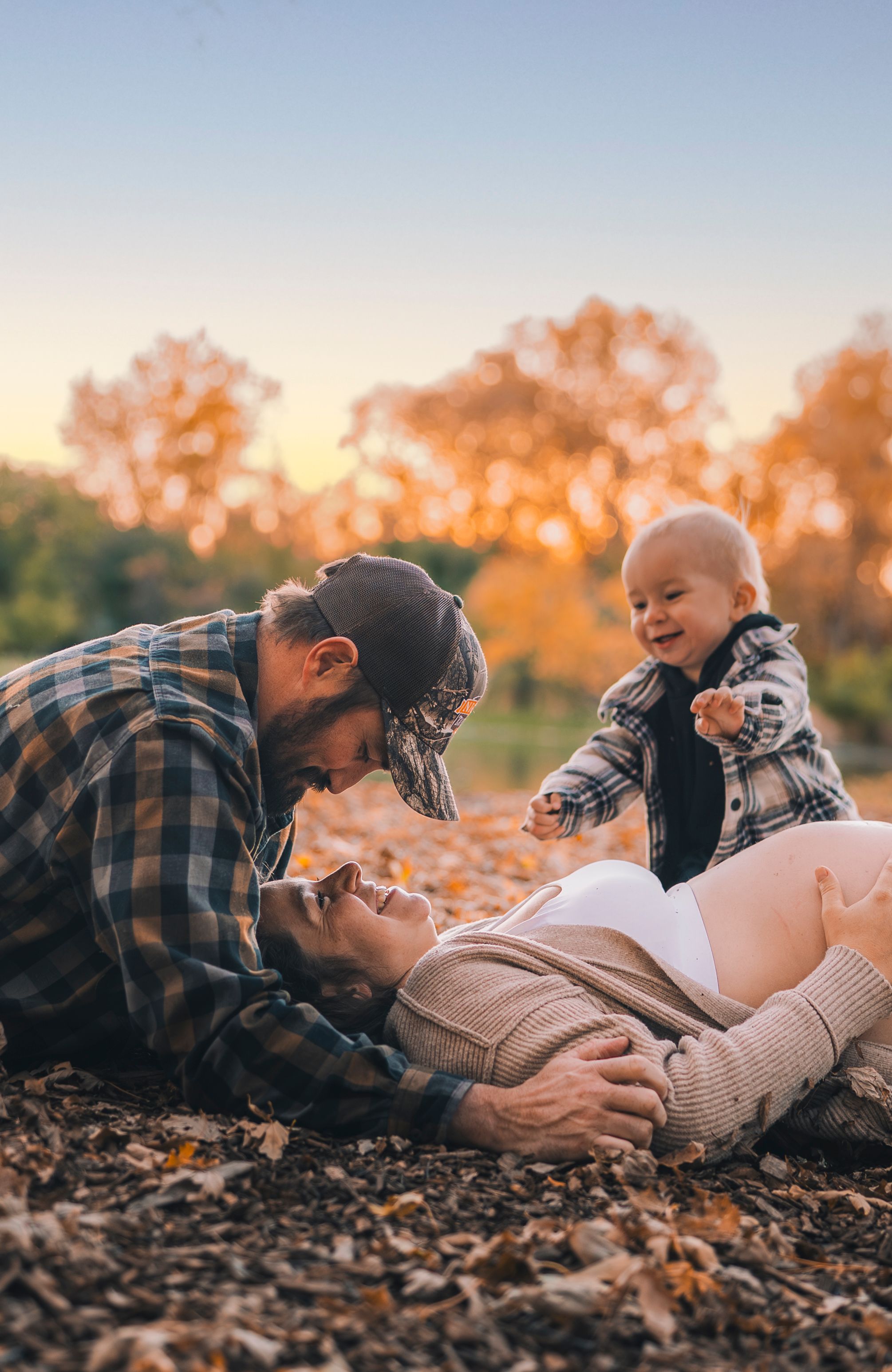 People laying together in autumn leaves during golden hour sunset creating intimate lifestyle portraits.