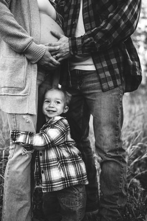A series of black and white photos showing a couple in casual clothing holding a small child in a plaid shirt.