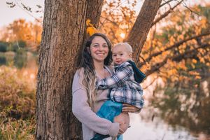 Mother and baby share tender moments in autumn forest setting with golden sunlight filtering through trees.