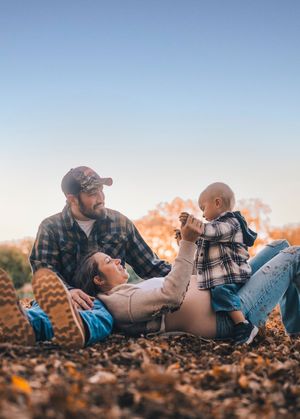 A family lies together on autumn leaves during a lifestyle photography session at sunset.