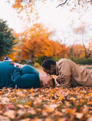 A person lies peacefully on a bed of vibrant orange autumn leaves during a fall photo session.