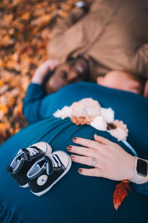 A hand rests on blue fabric with autumn leaves and baby shoes in a creative maternity photography composition.