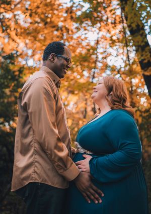 A couple shares an intimate moment together in a forest with warm autumn foliage glowing in the background.