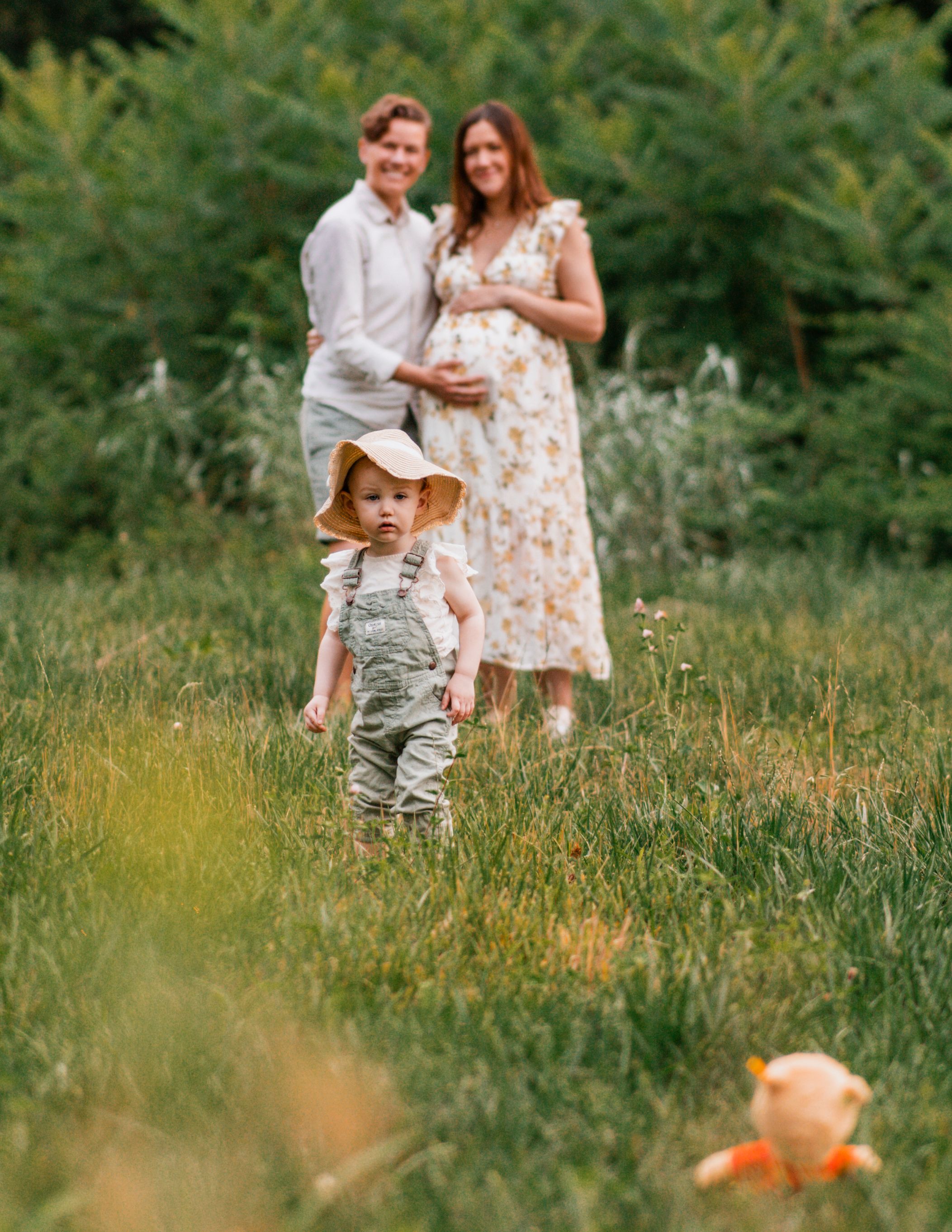 A family walks together through a sunlit meadow of tall grass and wildflowers on a summer afternoon.