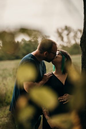 A romantic couple shares an intimate moment in a sunlit field with blurred yellow flowers in the foreground.