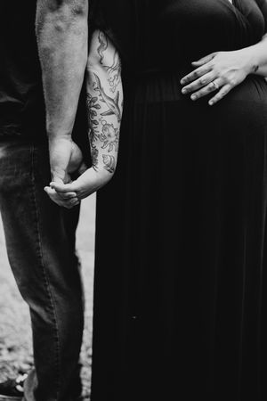 Black and white close-up of couple standing together showing detailed floral tattoo sleeve on one arm.