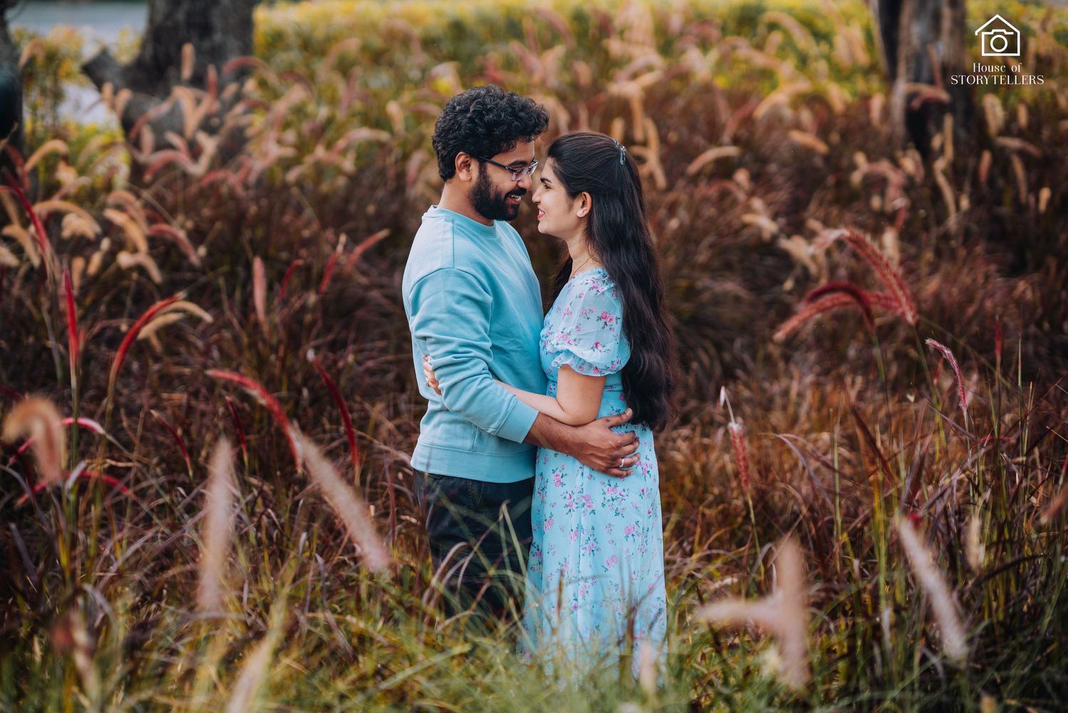 Couple in blue and light outfits share tender moment among tall grass.