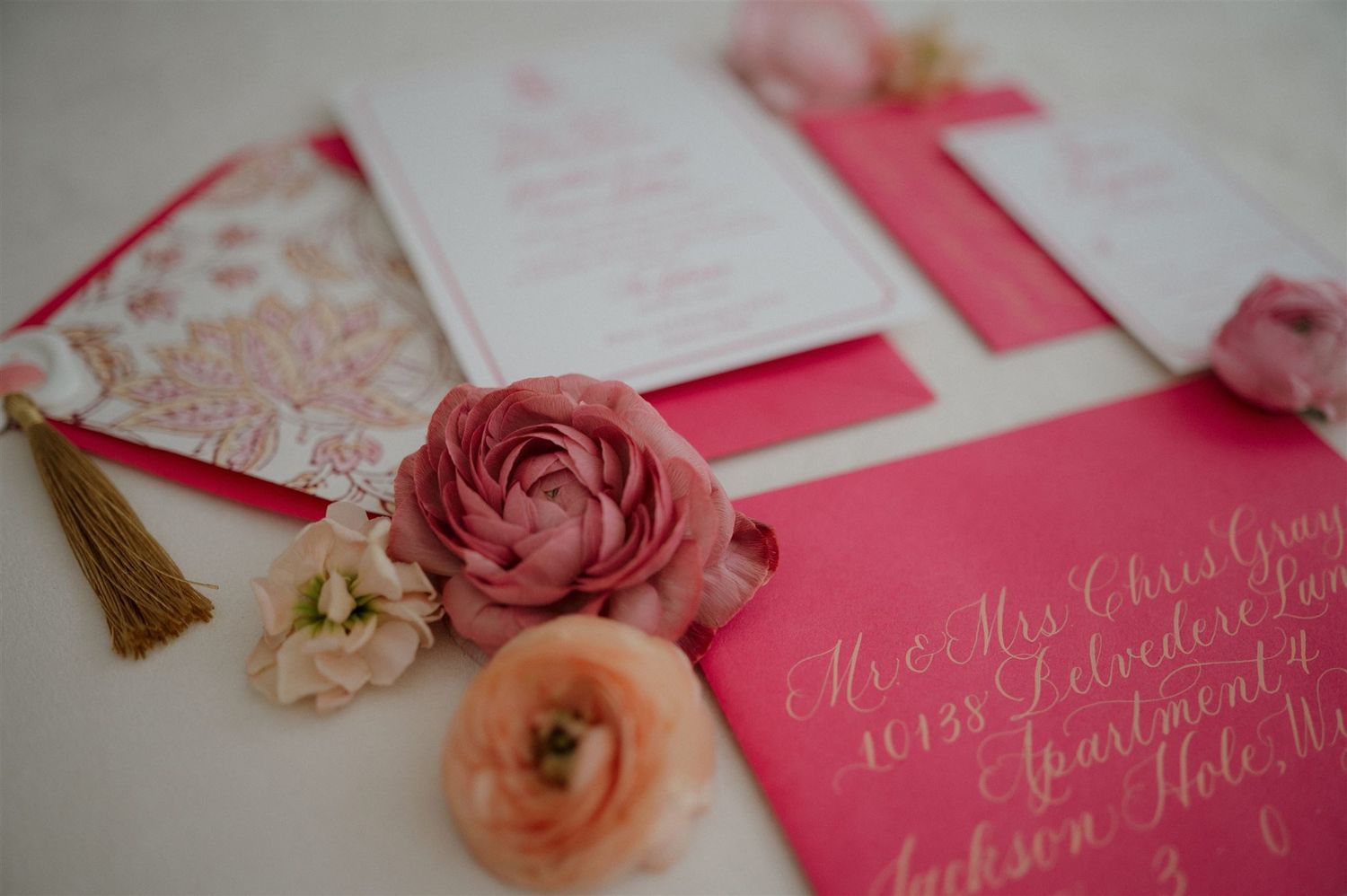 Pink wedding invitations with elegant calligraphy and floral accents arranged on a table.