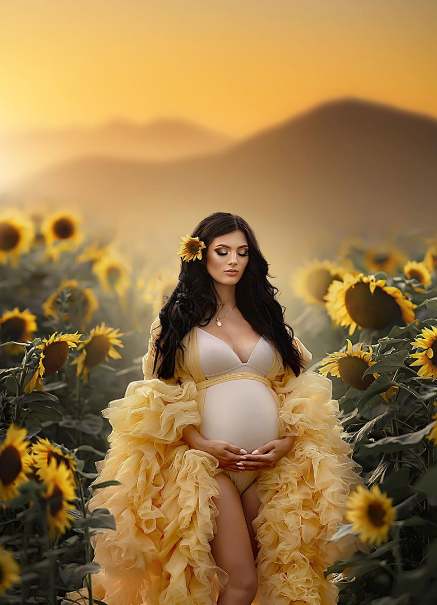 Dramatic sunset maternity photo in yellow ruffled robe surrounded by blooming sunflowers.