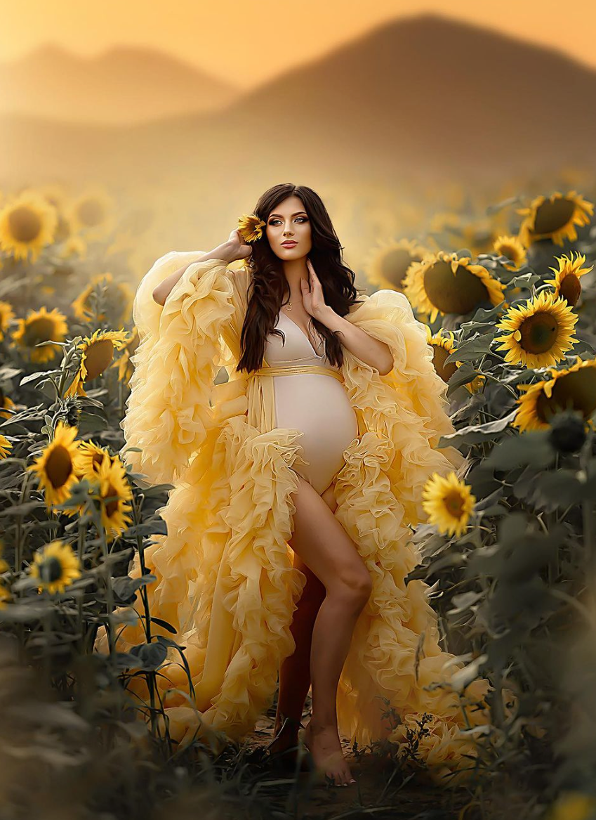 Ethereal maternity portrait in yellow ruffled robe amidst sunflower field at sunset.