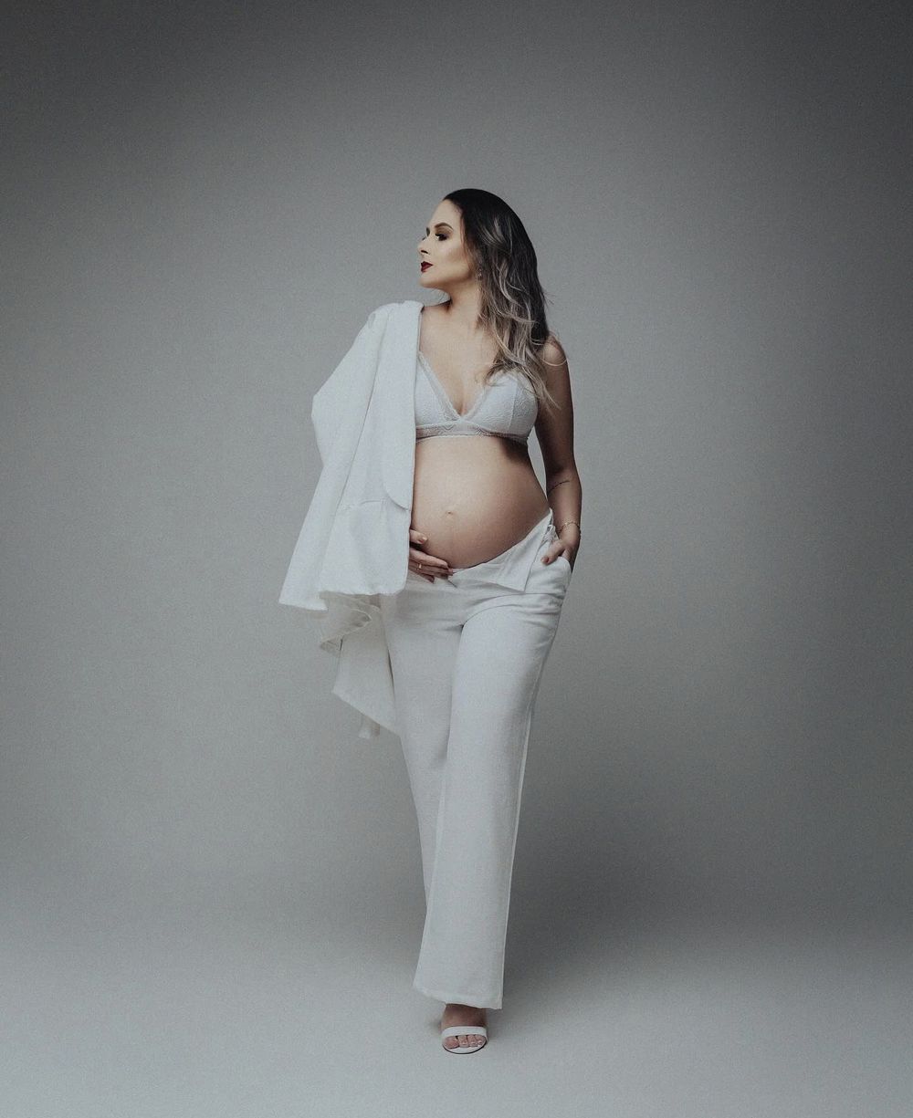 Maternity portrait of an expectant mother in white outfit with flowing fabric in studio setting.