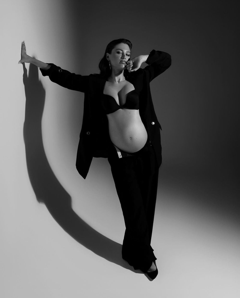 Artistic black and white maternity photo with dramatic shadow and open blazer.