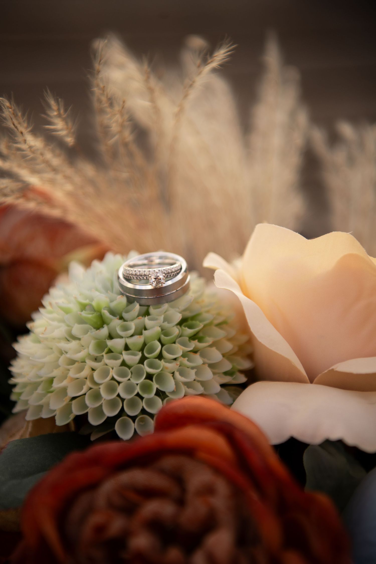 Wedding rings resting on a lush floral bouquet with roses and pampas grass in warm tones.