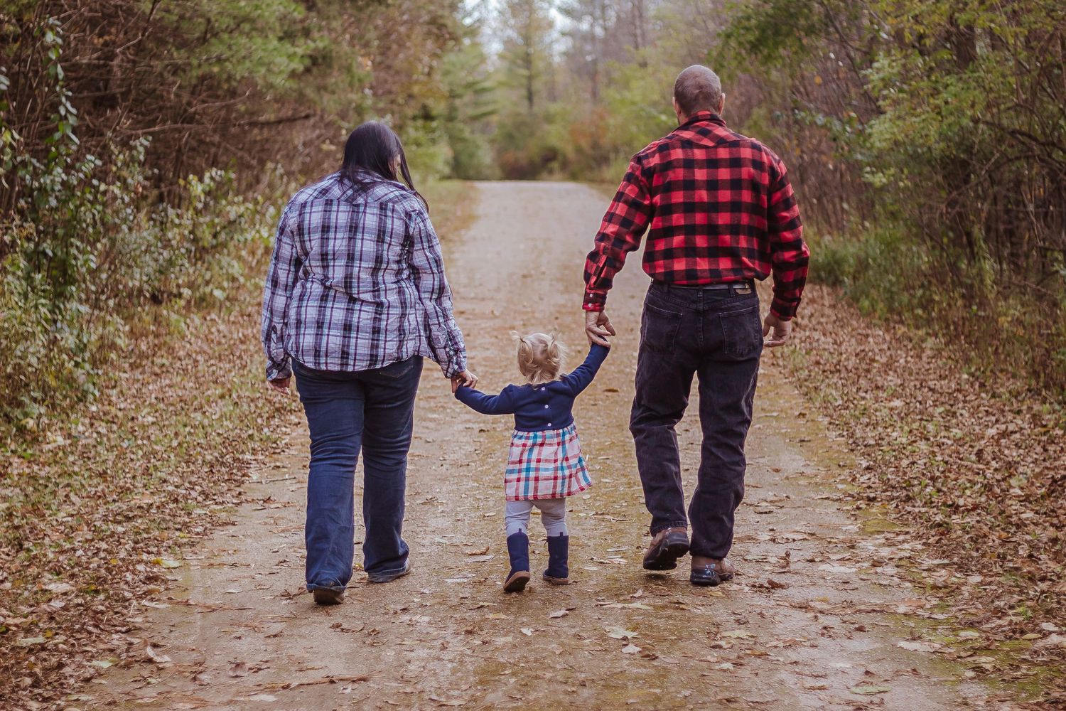 Family walking hand in hand down a leaf-covered path in autumn.