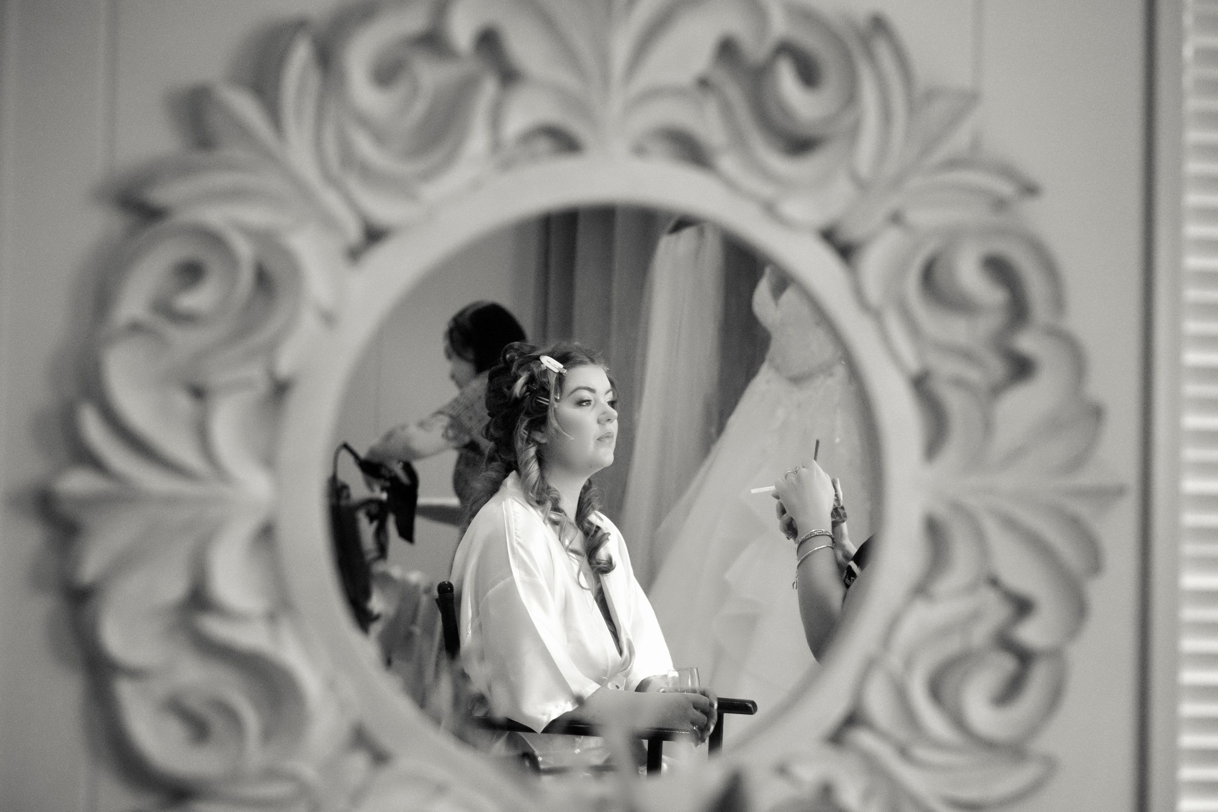 Black and white reflection in an ornate mirror showing bridal preparation.