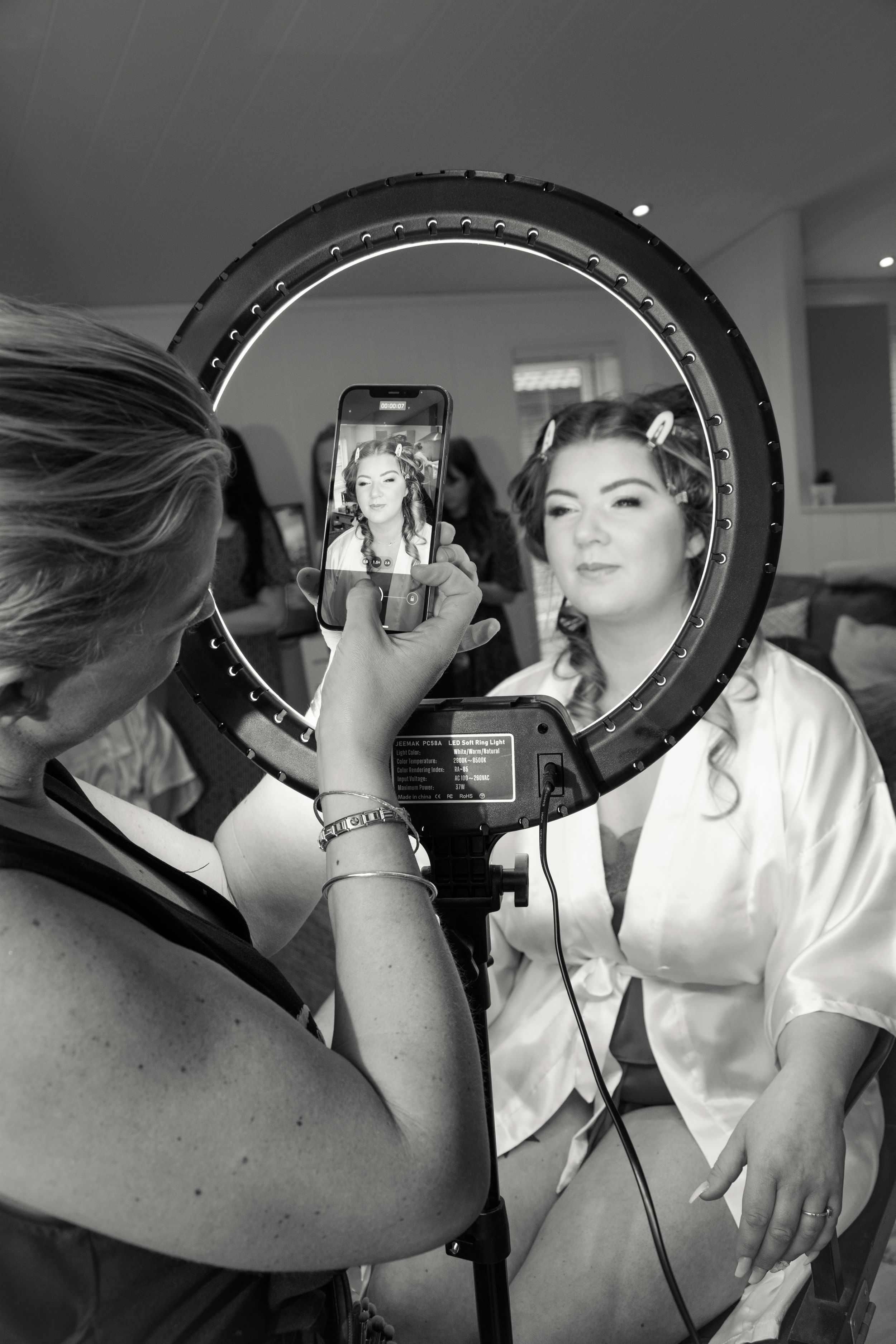 Behind-the-scenes photo of makeup application with a ring light and phone reflection.