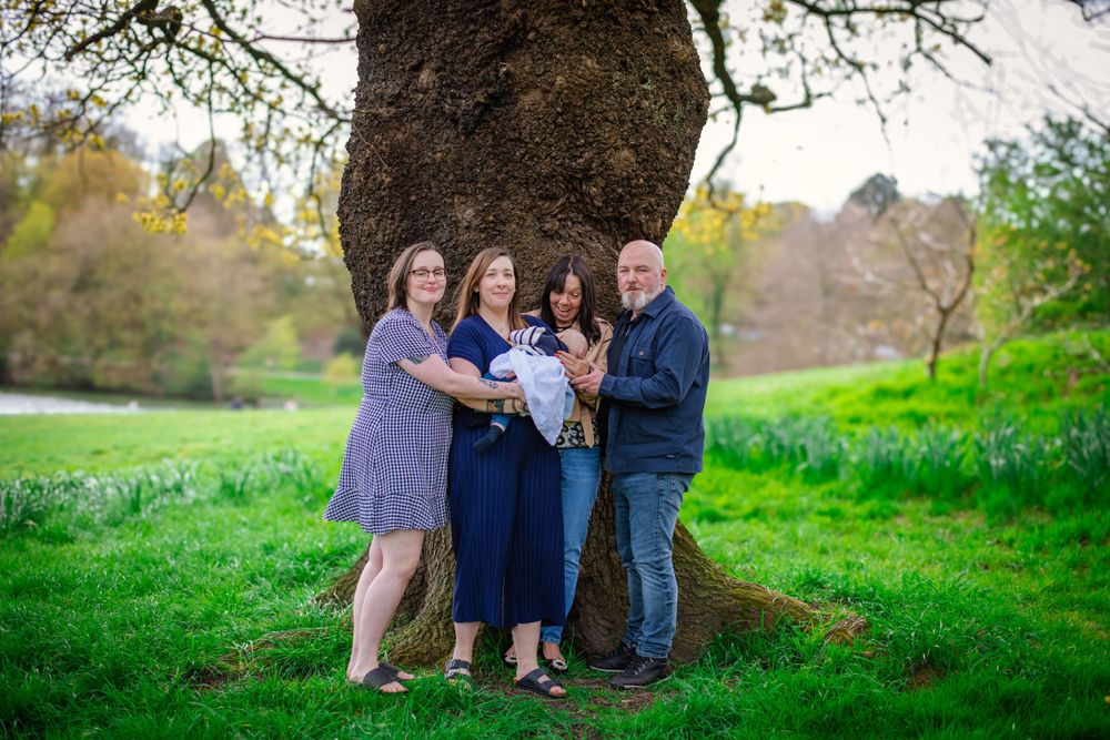 Family group portrait taken under large tree in green spring meadow.