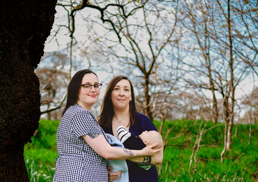 A joyful outdoor portrait with a small baby being held in front of blooming trees.