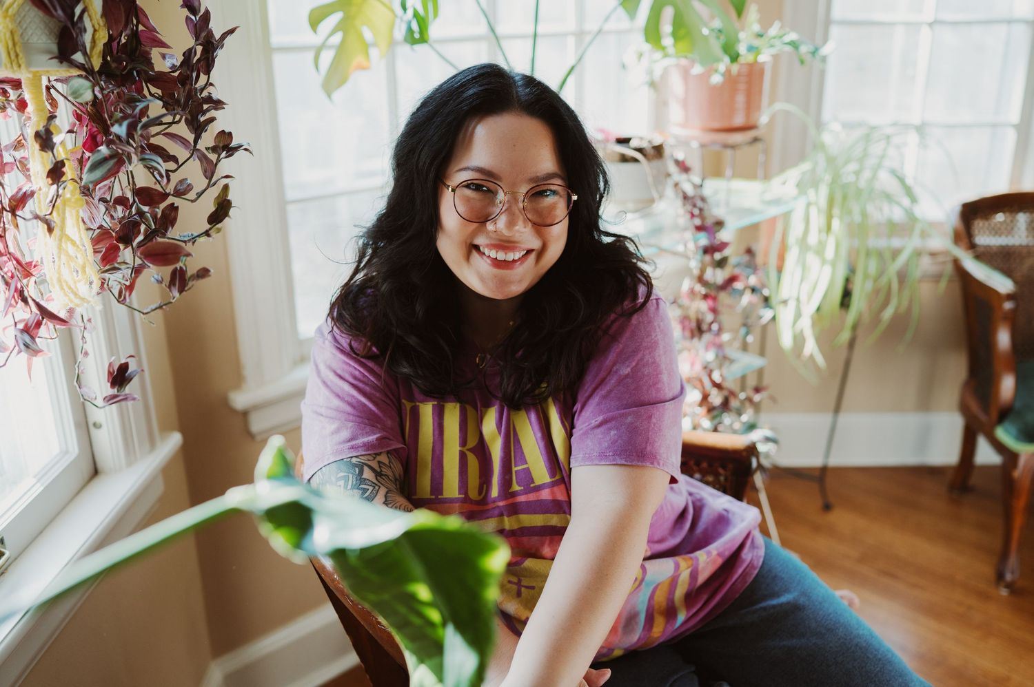 Person joyfully posing in garden with blooming purple flowers and greenery.