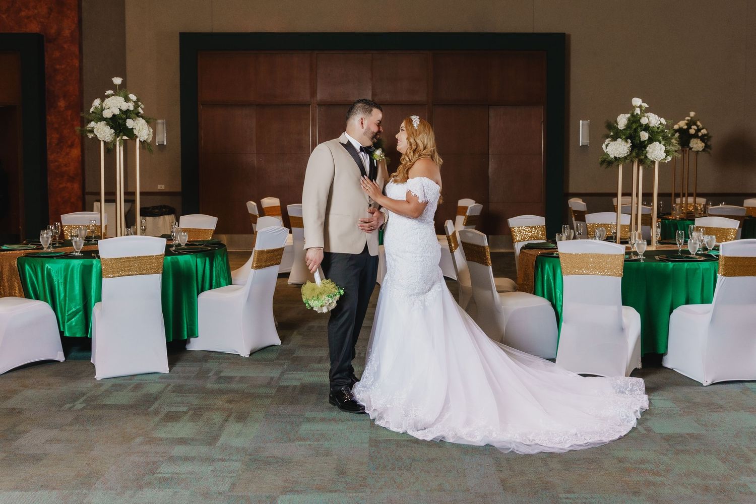 A reception venue with green and white decor featuring elegantly dressed couple in the center of the room.
