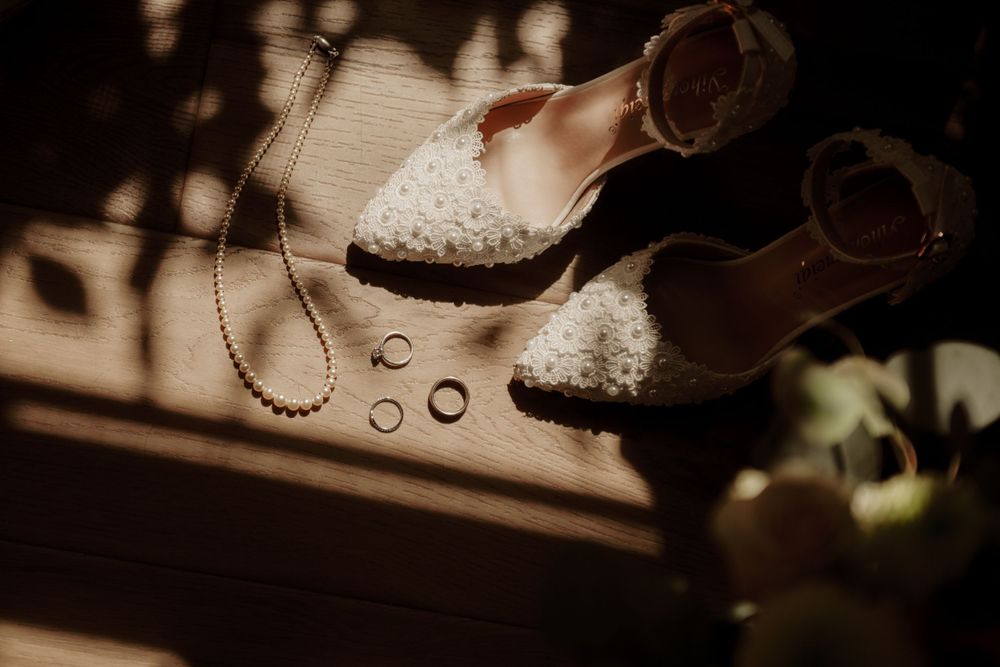 Wedding accessories including lace shoes and jewelry arranged artistically in moody lighting.