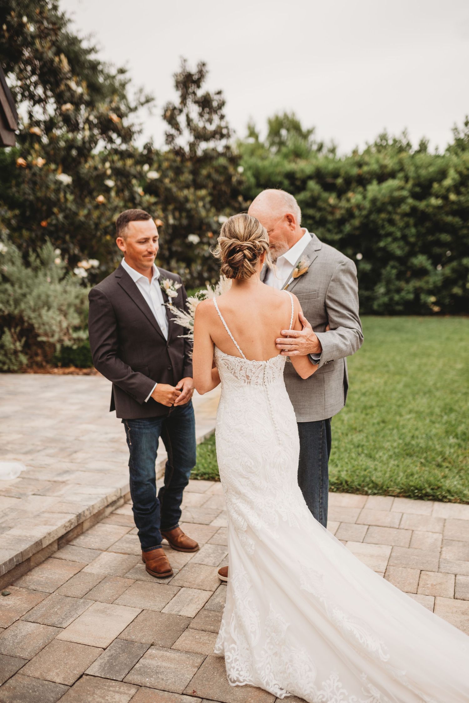 Wedding ceremony on stone patio with bride in fitted lace gown and two men in suits.
