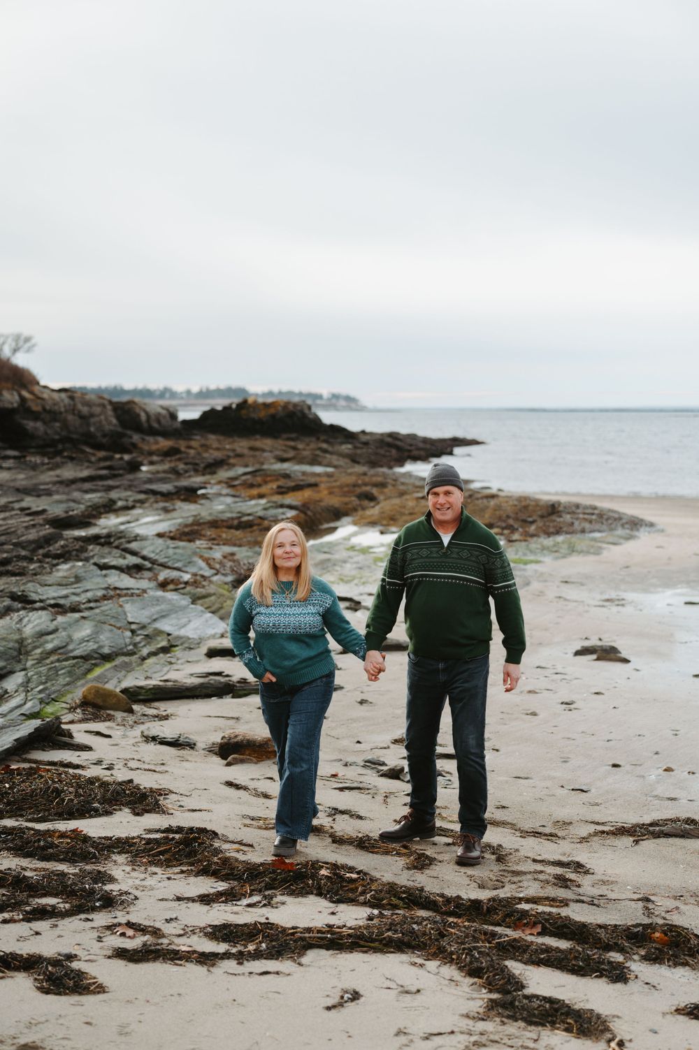 A couple walks together along a rocky beach shoreline on an overcast day.