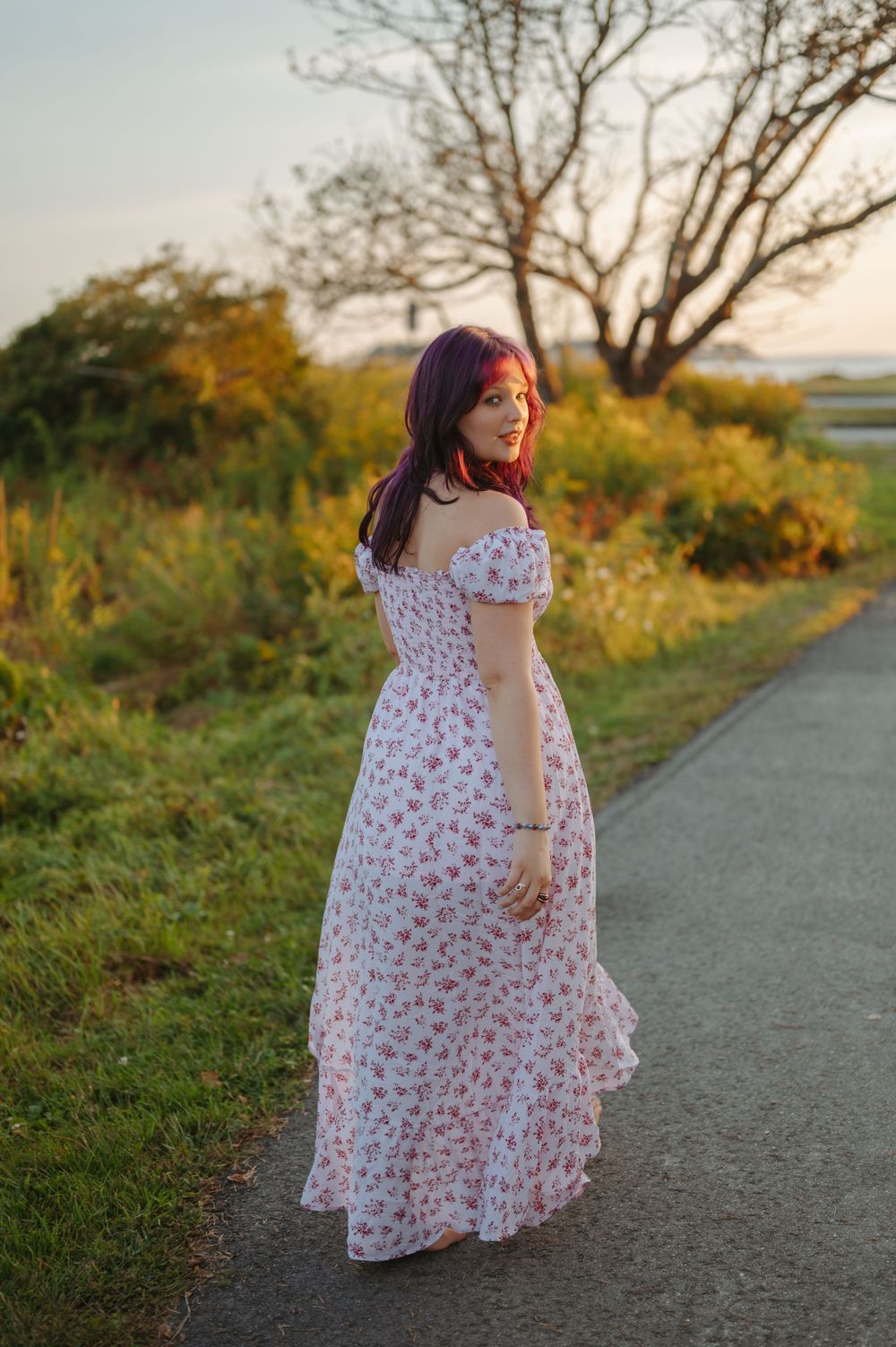 A flowing floral dress catches the golden sunlight on a countryside path during sunset.