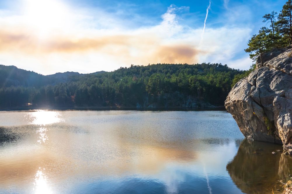 Tranquil lake with rocky cliff face reflecting in calm waters during sunset.
