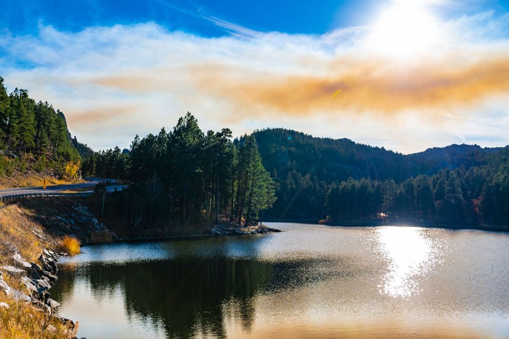 Serene mountain lake reflecting golden sunlight with evergreen forest surrounding the shoreline.