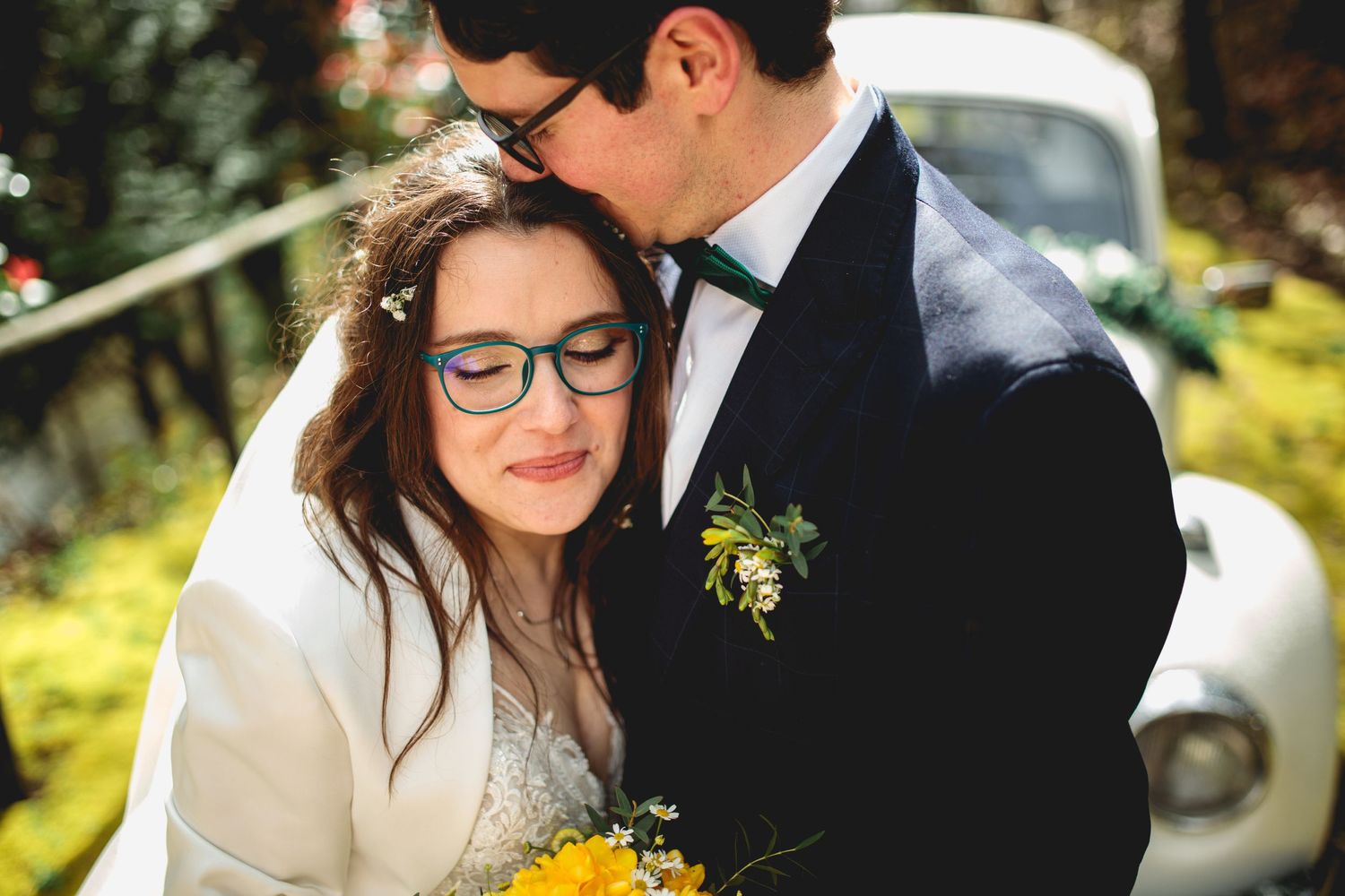 A romantic wedding photo with yellow sunflowers and a classic white car in the background.