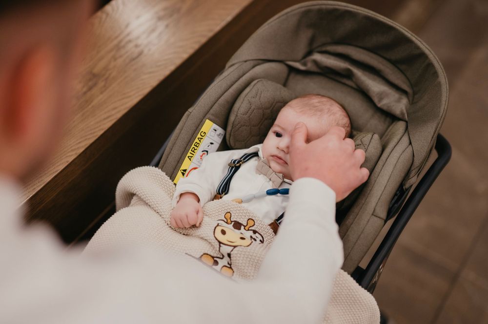 A baby rests in a car seat covered with a white blanket featuring a giraffe design.