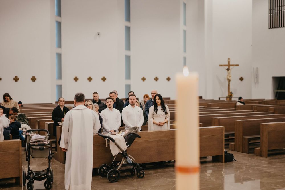 A church baptism ceremony with attendees seated in pews and a lit candle in the foreground.