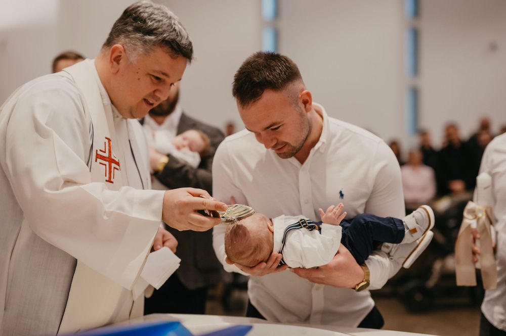 Two clergy members perform a baptism ceremony over an infant in a church setting.