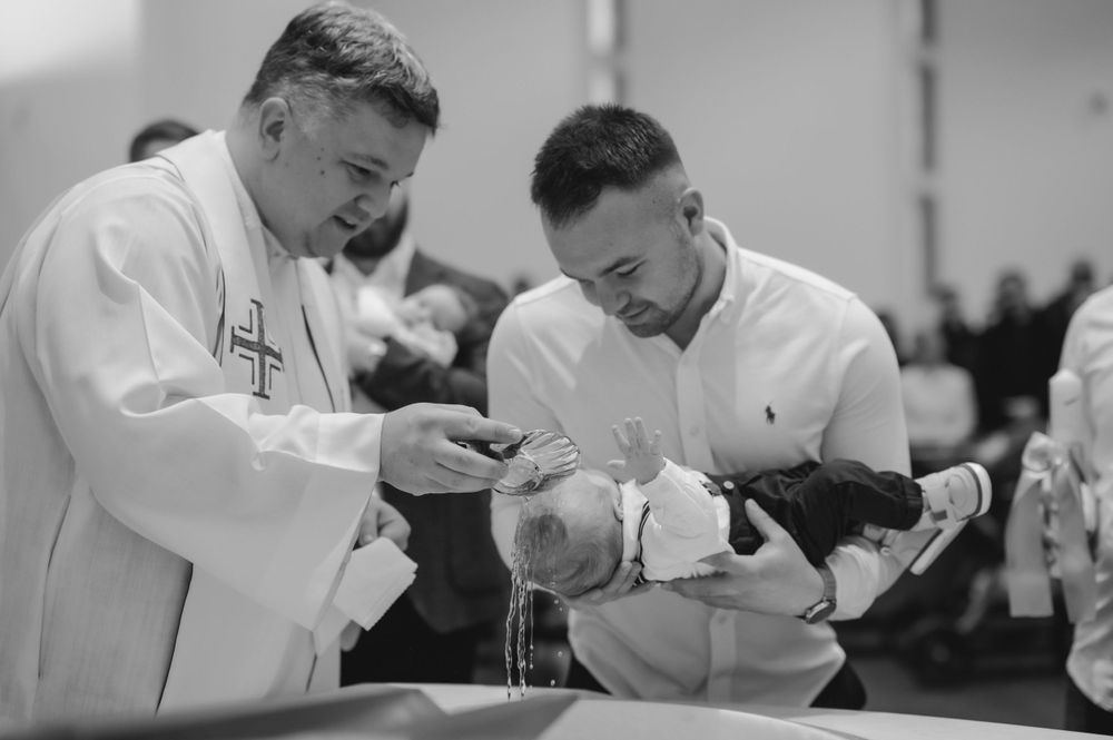 A black and white photo of a baptism ceremony being performed by two religious figures.