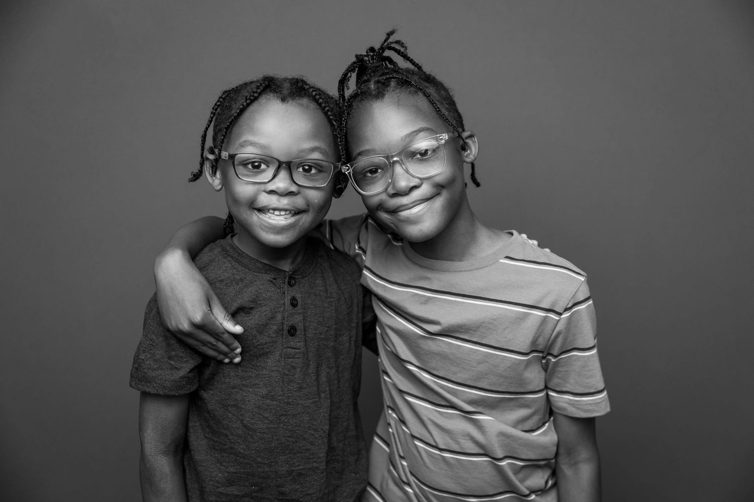 Black and white portrait of two children with glasses smiling together.