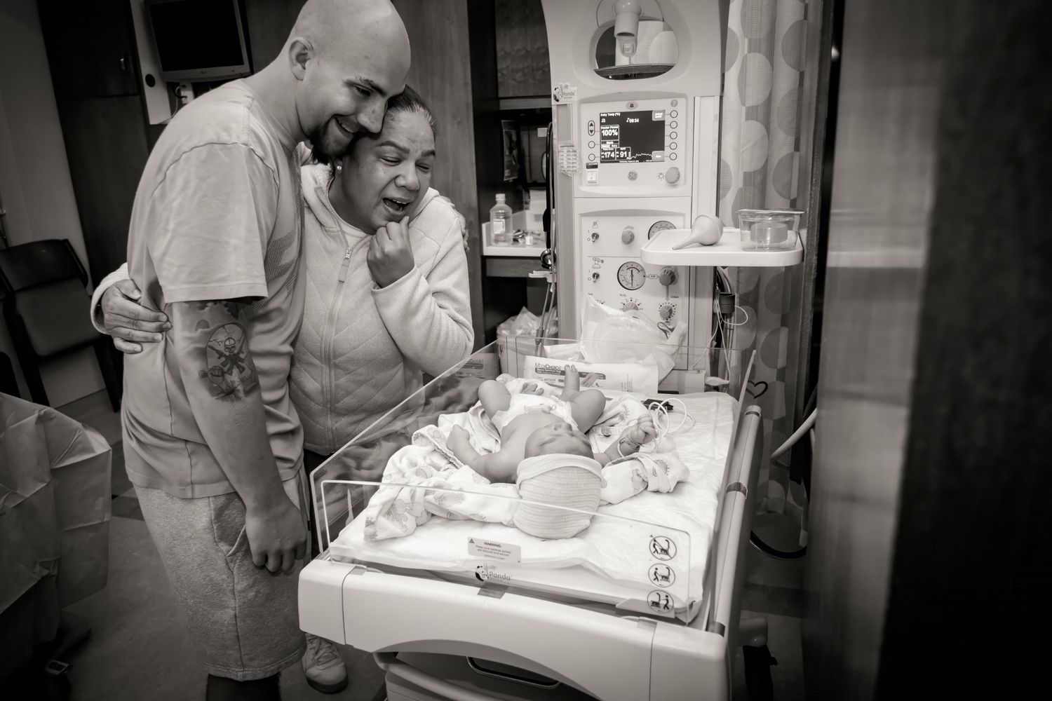 Black and white image of emotional moment in hospital NICU with newborn in incubator.