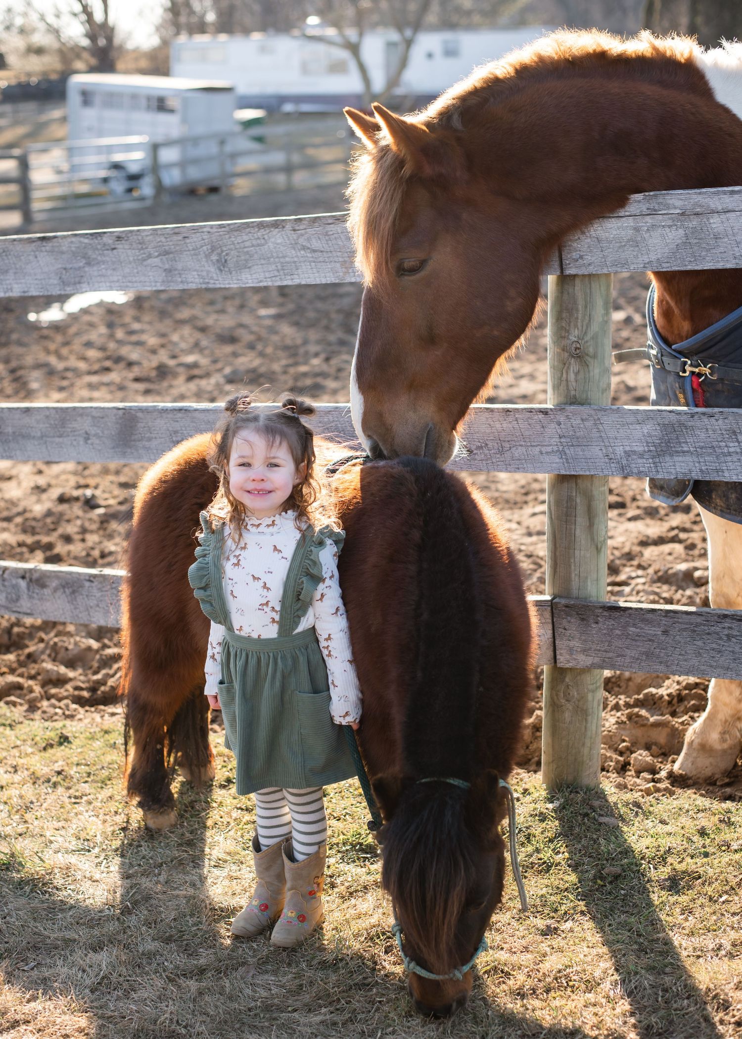 A gentle brown horse bends down to greet a small child by a wooden fence.
