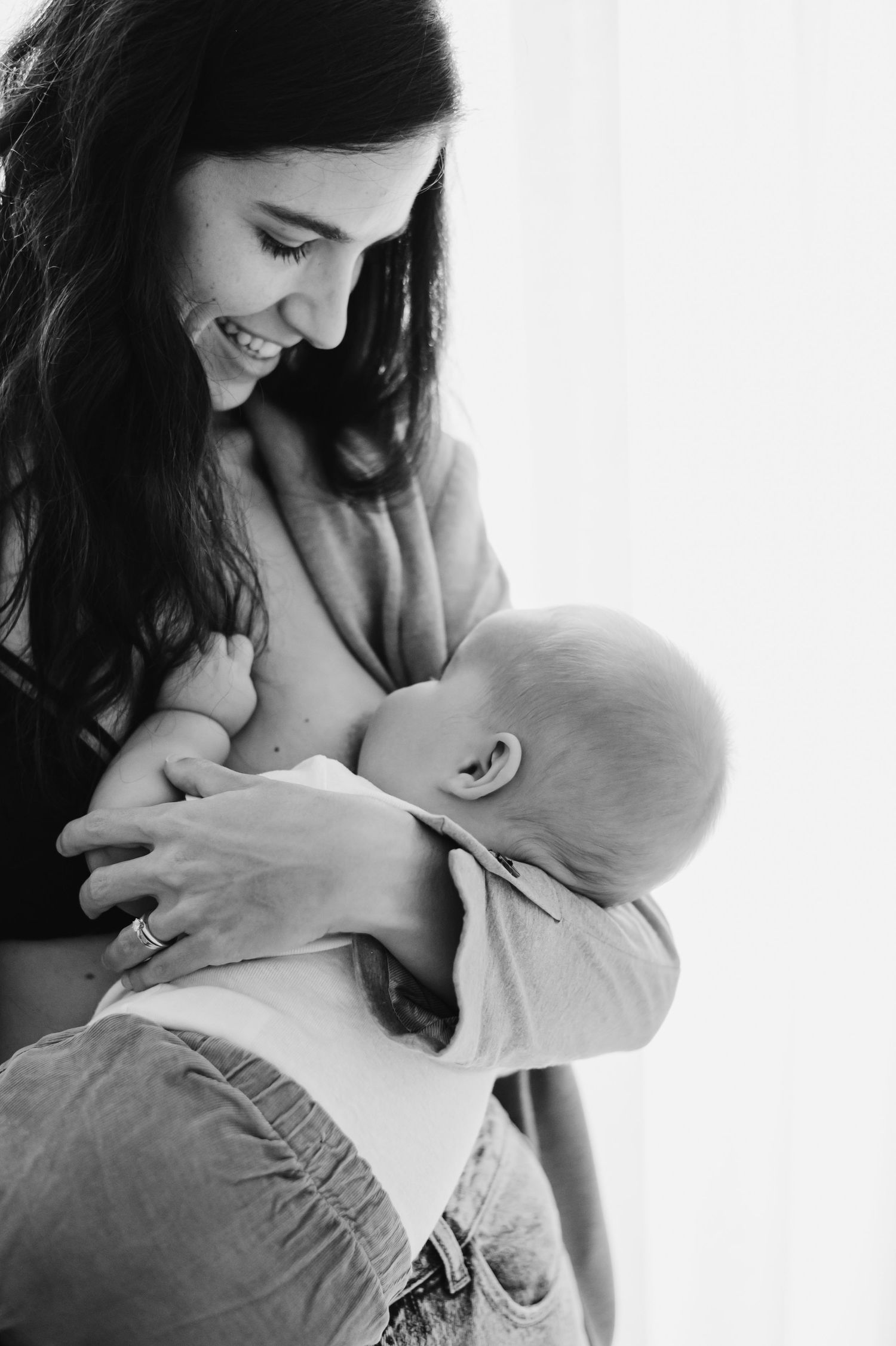 Black and white intimate portrait of mother nursing baby against white background.
