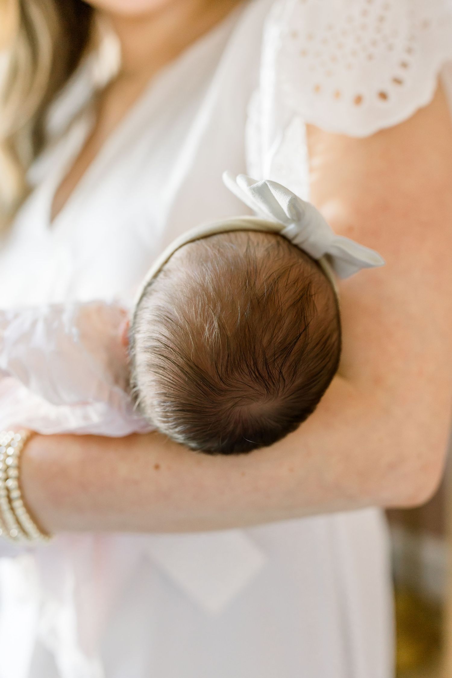 Close-up of a newborn baby's head with dark hair being cradled in arms wearing white lace.