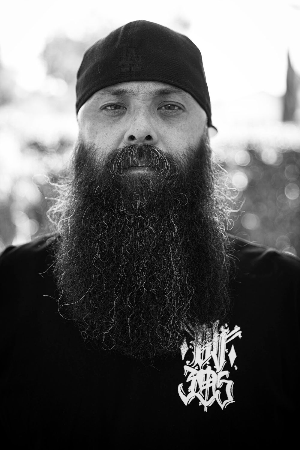 Black and white close-up profile shot featuring a long beard and baseball cap.